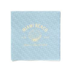 a blue towel with the words miami beach on it and a shell in gold lettering