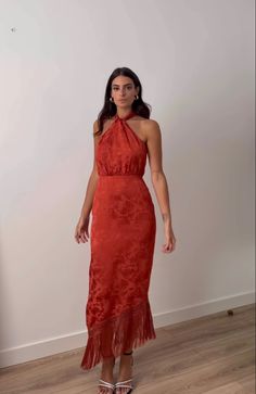 a woman standing in front of a white wall wearing a red dress with fringes