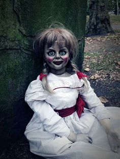 a creepy doll sitting on the ground in front of a tree with its eyes wide open