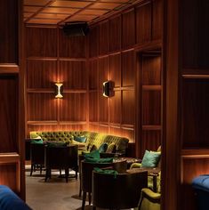 a room filled with lots of furniture and wooden paneling on the walls, along with green velvet chairs