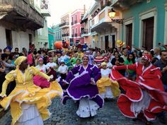 several people in colorful dresses are dancing on a cobblestone street while others watch