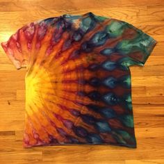 a t - shirt that has been dyed with different colors and patterns on it, sitting on a wooden floor