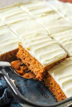 carrot cake with white frosting in a glass dish on top of a blue cloth