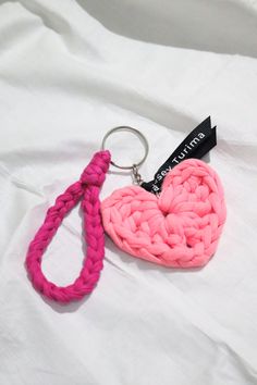 a pink heart shaped keychain sitting on top of a white sheet with a black tag