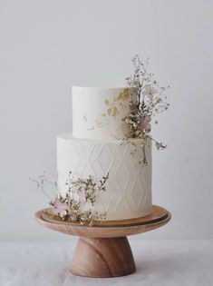 a three tiered white cake with pink flowers on the side and gold leaf decoration