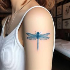 a blue dragonfly tattoo on the left upper arm and right lower arm, is shown in front of a woman's white tank top