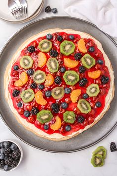 a fruit pizza with kiwis, oranges and blueberries on it sitting on a plate