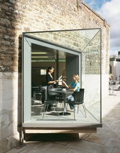 two people sitting at a table in front of a glass enclosed room with brick walls