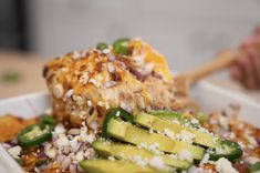 a close up of a bowl of food with cucumbers and cheese on top