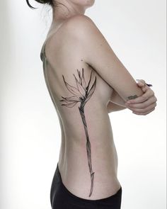 a woman with a flower tattoo on her back and shoulder, standing in front of a white background