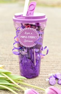 a purple cup filled with lots of candies next to tulips and flowers