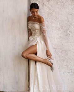 a woman in a white dress leaning against a wall with her leg up on the ground