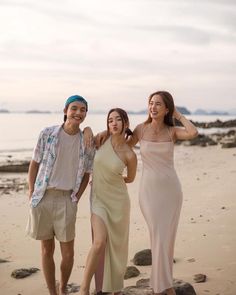 three people are standing on the beach posing for a photo with one woman wearing a dress