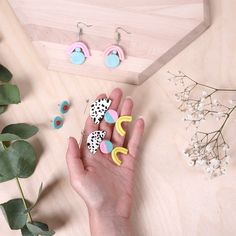 a person's hand is shown with earrings on it and some flowers in the background