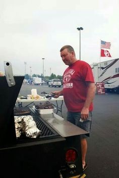 a man standing next to a grill in a parking lot