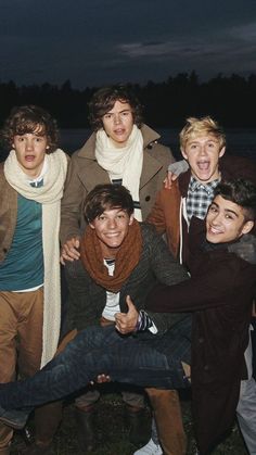 four young men posing for a photo in front of the water at night with their hands on their hipss