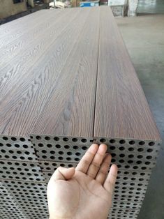 a person holding their hand up to the top of a piece of wood that has holes in it