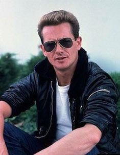 a man sitting on the ground with his hands in his pockets and wearing black sunglasses