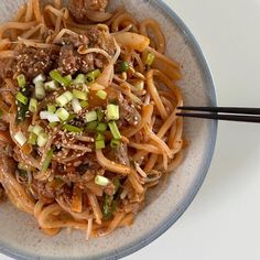 a bowl filled with noodles and meat on top of a white table next to chopsticks