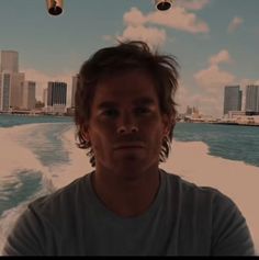 a man standing on top of a boat in the ocean next to tall buildings and water