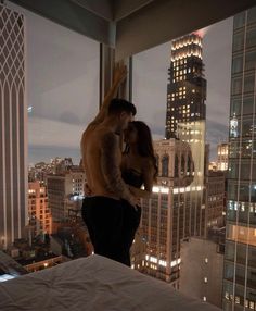 a man and woman standing on top of a bed in front of a cityscape