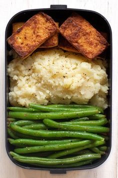 a container filled with mashed potatoes, green beans and fried tofu pieces on top