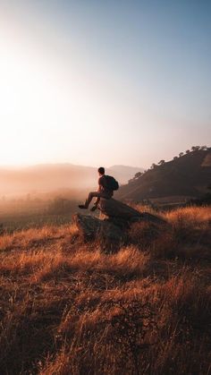 a man sitting on top of a rock in the middle of a dry grass field