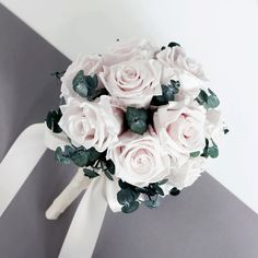 a bridal bouquet with white roses and greenery on the side of a striped wall