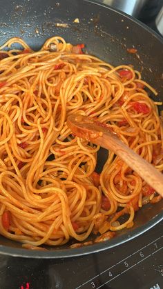 spaghetti being cooked in a wok on top of the stove with a wooden spoon