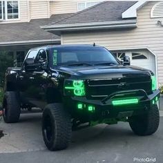 a black truck parked in front of a house with green lights on it's headlights