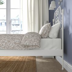 a white bed sitting in a bedroom next to a window with curtains on the windowsill