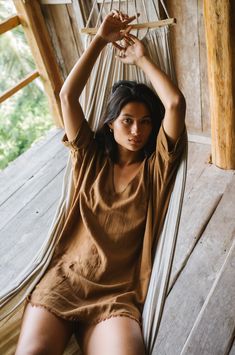 a woman sitting in a hammock with her hands above her head and looking at the camera