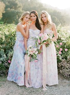 three beautiful women standing next to each other in front of some bushes and pink flowers