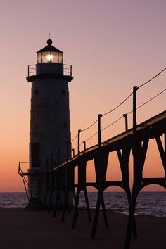 a light house sitting on top of a wooden pier next to the ocean at sunset