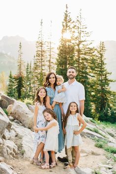 a family posing for a photo on the side of a mountain with pine trees in the background