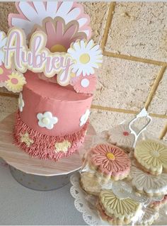 there is a pink cake and some cookies on the table next to eachother