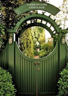 a green gate that is surrounded by bushes and trees, with the entrance to a garden