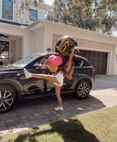 a woman is holding balloons and standing next to a car in front of a house