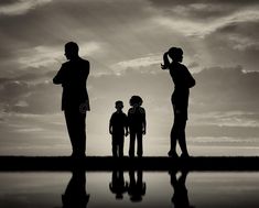 silhouettes of three people standing in front of a body of water