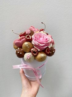 a hand holding a cup filled with chocolate covered donuts and pink roses in it