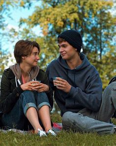 two people are sitting on the grass and one is holding a cell phone in his hand