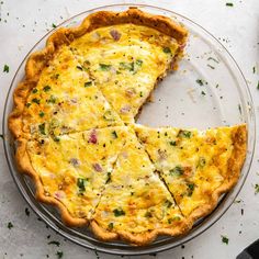 a cheesy quiche on a glass platter with one slice cut out