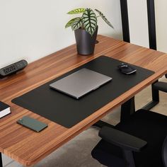 a desk with a laptop, mouse and cell phone on it next to a potted plant