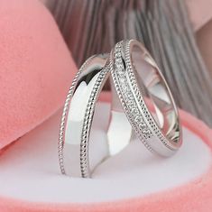 two white gold wedding rings with diamonds on top of pink velvet cushioned surface, close up