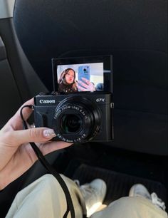 a person holding up a camera in their hand while sitting in the back seat of a car