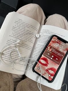 an open book with headphones on it next to a cell phone and earbuds