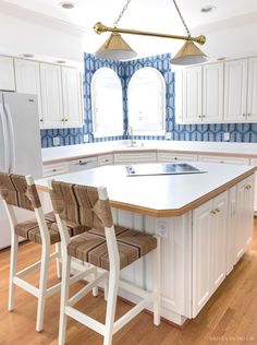 a kitchen with white cabinets and an island in the middle, two chairs on each side