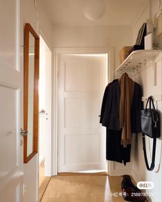 a white hallway with a coat rack, shoes and handbag on the shelf next to it