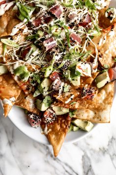 a white plate topped with nachos covered in cheese and toppings on top of a marble table