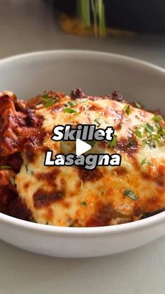 a white bowl filled with lasagna covered in sauce and cheese, on top of a table